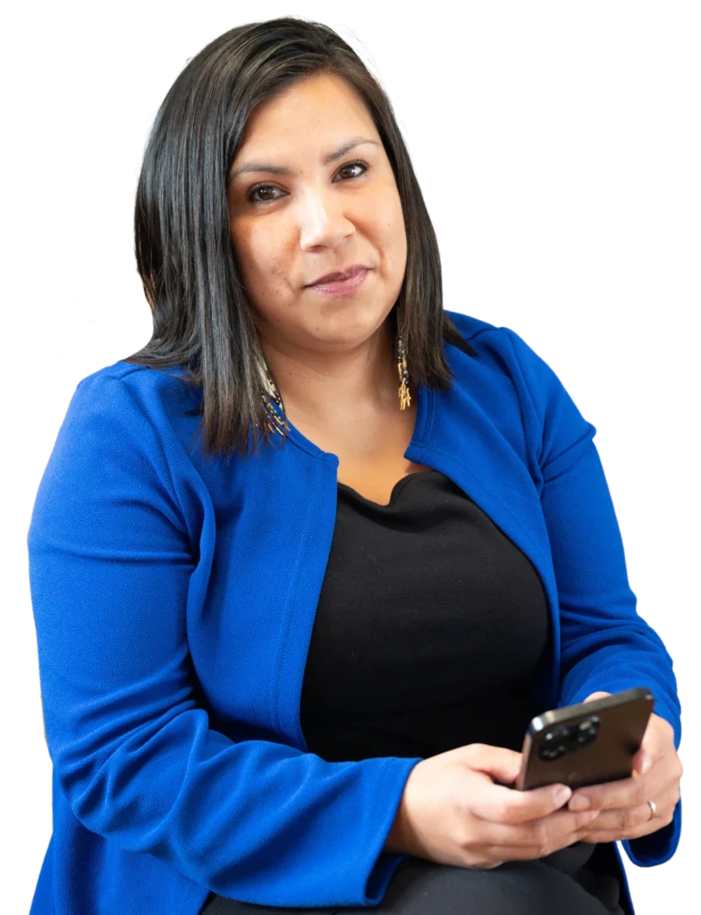 Kanessa Michel, une femme Innue, vêtue d'une veste bleue et d'un haut noir, tenant un téléphone portable et regardant la caméra.